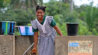 Die zwölfjährige Marie-Rose steht mit einem Eimer Wasser am neuen Brunnen auf dem Gelände ihrer Schule in Guinea.