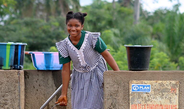 Die zwölfjährige Marie-Rose steht mit einem Eimer Wasser am neuen Brunnen auf dem Gelände ihrer Schule in Guinea.