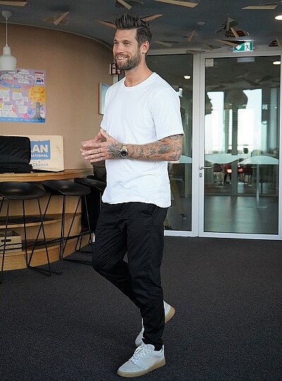 Jan Möller steht in einem weiten Raum und begrüßt die Schüler lächelnd