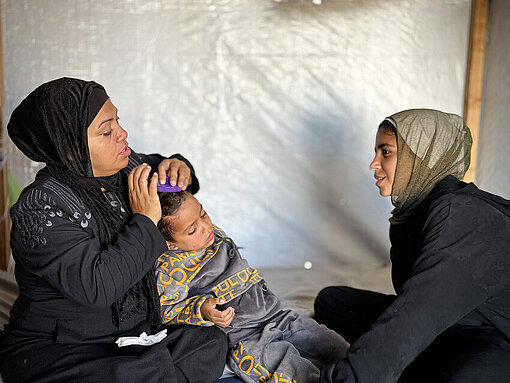 Eine Mutter aus Gaza mit ihren Kindern zwei Kindern, eine junge Frau und ein kleiner Junge, sitzen in einem Zelt auf dem Boden 