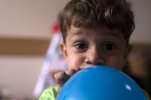 Spieltherapie Ein Junge schaut in die Kamera und bläst einen Luftballon auf