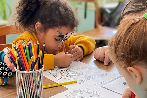 In einem geschützen Raum können Kinder mit Buntstiften malen Zwei junge Mädchen malen mit Buntstiften