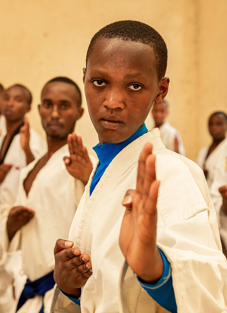 Eine Gruppe Jugendlicher in Karate-Anzügen schaut konzentriert in die Kamera, Hände gehoben.