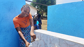 Eine junge Frau freut sich über die neue Wasserstelle mit Trinkwasser in ihrer Gemeinde.