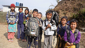 Grundschulkinder mit Rucksäcken lächeln in die Kamera. 