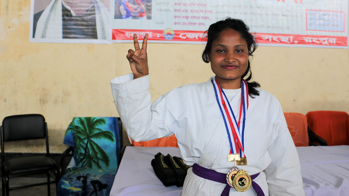 Eine Karateka trägt eine Goldmedaille und zeigt ein Peace-Zeichen