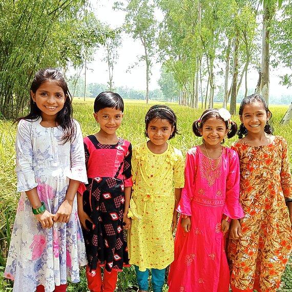 Fünf Kinder in bunter Kleidung stehen lächelnd in einer Reihe vor einem Feld