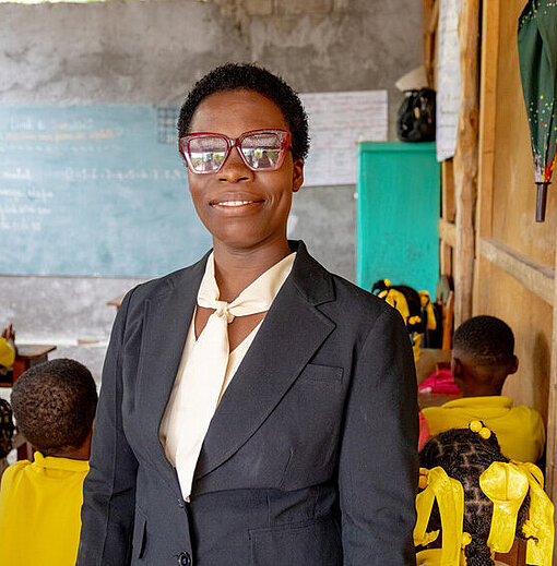 Rose ist mit Leib und Seele Lehrerin Eine Lehrerin lächelt in die Kamera, während die Klasse mit dem Rücken zu ihr sitzt