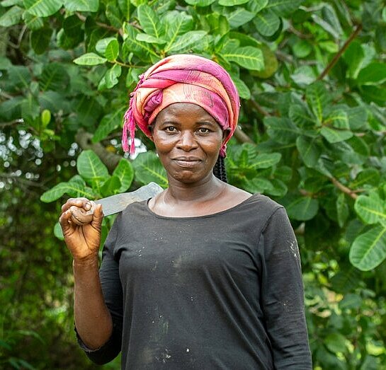 Anna hatte die Möglichkeit, in eine Cashewfarm zu investieren Frau vor Cashewfarm stehend