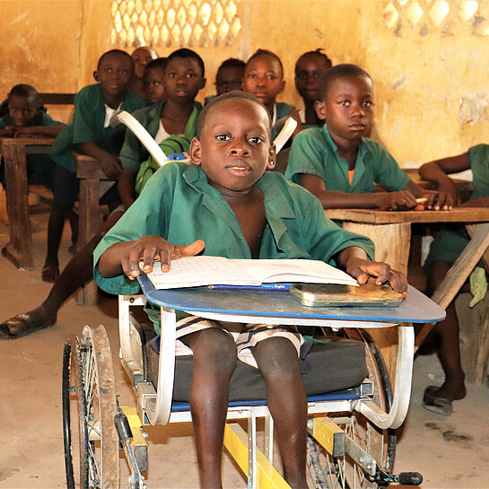 Ein Junge im Rollstuhl sitzt ganz vorne in einer Schulklasse