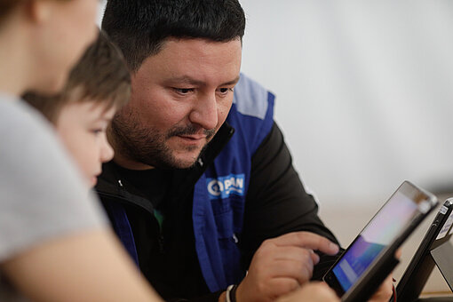 Ein Plan-Mitarbeiter unterstützt zwei Kinder beim Lernen am Tablet Ein Plan-Mitarbeiter unterstützt zwei Kinder beim Lernen am Tablet