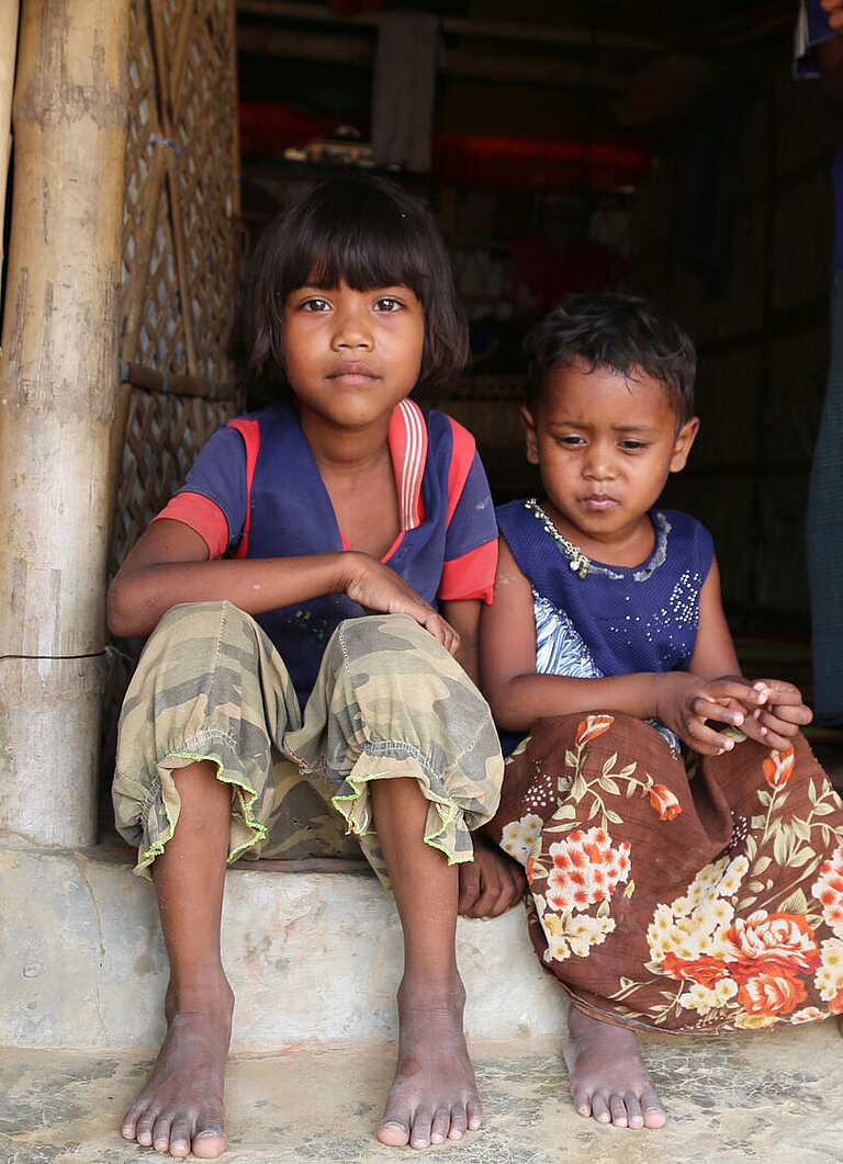 Ein Mädchen und ein kleiner Junge sitzen in einem Gebäudeeingang.