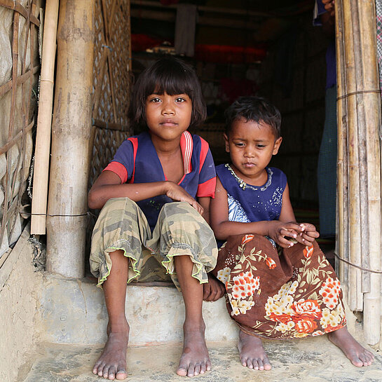 Ein Mädchen und ein kleiner Junge sitzen in einem Gebäudeeingang.