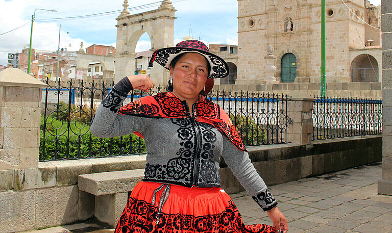 Jessica aus Chumbivilcas, Peru, steht vor einer historischen Kirche und zeigt stolz ihre Stärke, während sie traditionelle Kleidung trägt.