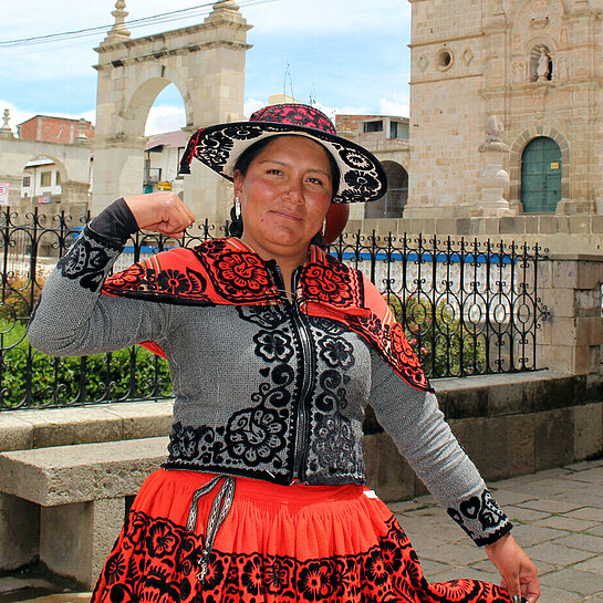 Jessica aus Chumbivilcas, Peru, steht vor einer historischen Kirche und zeigt stolz ihre Stärke, während sie traditionelle Kleidung trägt.