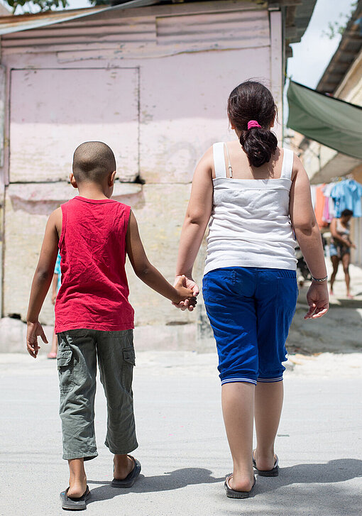 Ein kleiner Junge und ein etwas größeres Mädchen gehen Hand in Hand, den Rücken zur Kamera.