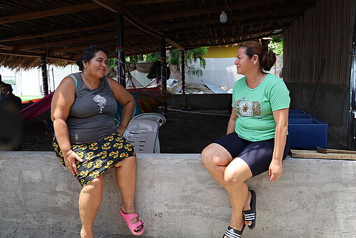 Zwei Frauen sitzen auf einer kleinen Mauer und sind in ein Gespräch vertieft