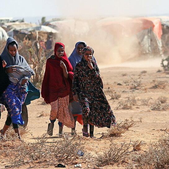 Eine Gruppe somalischer Mädchen laufen über staubtrockene Erde durch ein Camp für Binnengeflüchtete