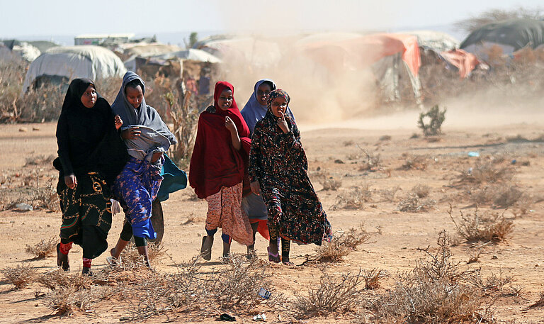 Eine Gruppe somalischer Mädchen laufen über staubtrockene Erde durch ein Camp für Binnengeflüchtete