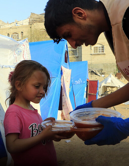 Warmes Essen für Kinder in Gaza, zubereitet von der Plan-Partnerorganisation Taawon Ein Helfer verteilt Speisen an Kinder