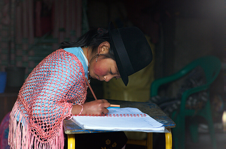Ein Mädchen sitzt an einem Tisch, beugt sich über eine Schulheft und schreibt etwas hinein