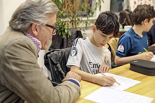 Zwei Kinder arbeiten mit einem grauhaarigen Mann an einem Schreibtisch