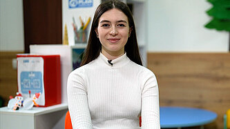 Eine junge Frau sitzt auf einem Stuhl und schaut lächelnd in die Kamera