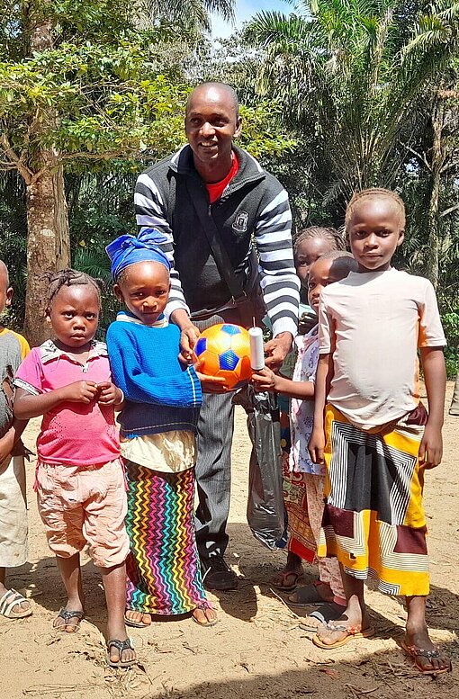 Tamba Michel (Mitte) war früher ein Plan-Patenkind – und unterstützt heute die jüngere Generation Ein junger Mann steht umringt von Kinder auf dem Schulhof