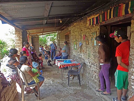Blick auf eine überdachte Veranda vor einem Haus aus Ziegeln, vor dem mehrere Personen auf Einlass warten