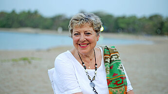 Eine Frau in weißer Bluse sitzt lächelnd in einem Stuhl