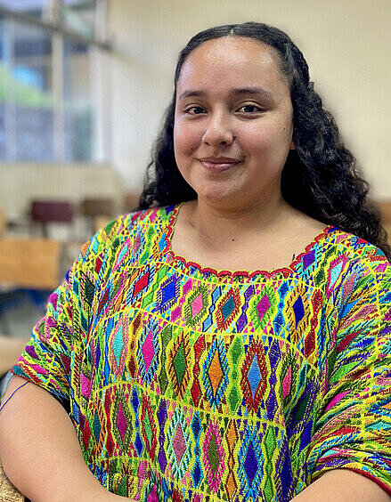 Jaqueline sitzt in einem Klassenzimmer und schaut aufmerksam nach vorne.