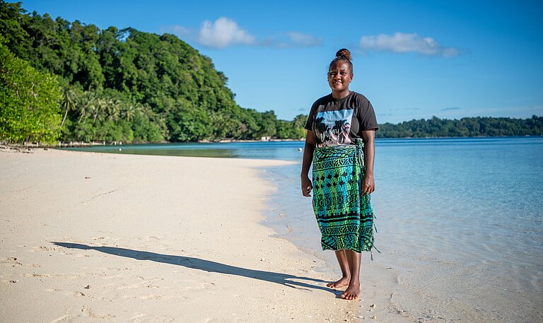Jayleen steht am Strand ihres Zuhauses auf Nggatokae