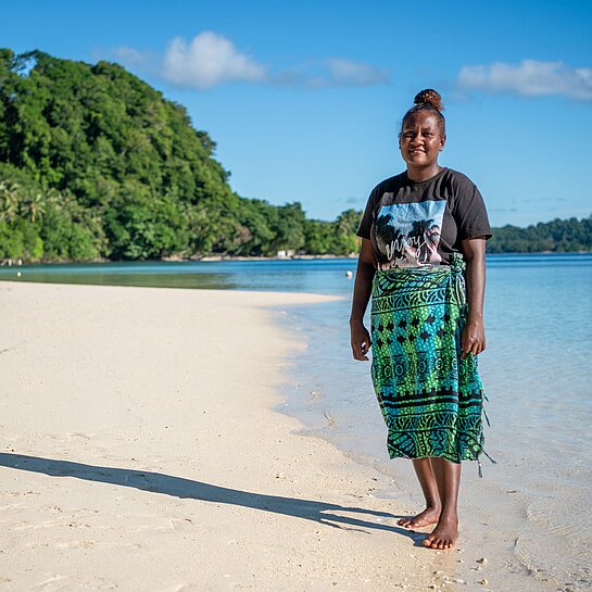Jayleen steht am Strand ihres Zuhauses auf Nggatokae