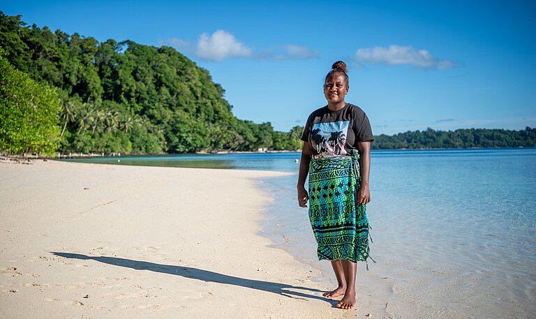 Jayleen steht am Strand ihres Zuhauses auf Nggatokae