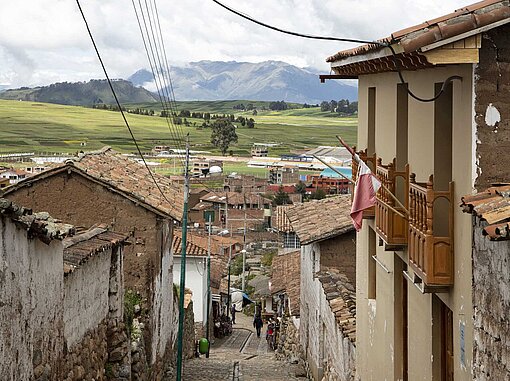 Blick auf eine Dorfstraße aus Kopfsteinpflaster mit geziegelten Häusern beiderseitig und Hügelketten am Horizont