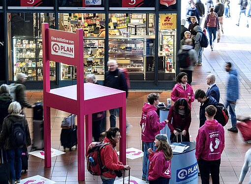 Mitglieder der Plan-Aktionsgruppe erklärten den interessierten Passant:innen, was es mit dem pinken Stuhl am Hamburger Hauptbahnhof auf sich hatte Riesiger pinker Stuhl in der Wandelhalle des Hamburger Hauptbahnhofs