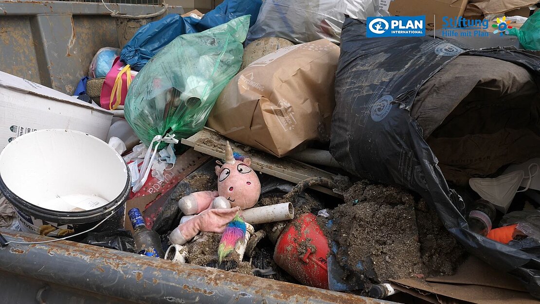 Ein Müllcontainer, in dem unter anderem ein schlammiges Einhorn-Kuscheltier liegt