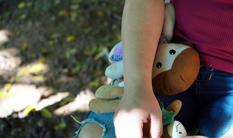 Nahaufnahme einer Person, die ihre Hand auf ihrem Bein abgelegt hat und unter dem Unterarm klemmt eine Stoffpuppe