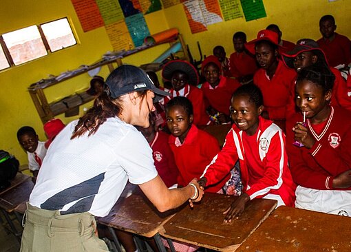 Frau gibt einem Mädchen die Hand, das an einer Schulbank sitzt