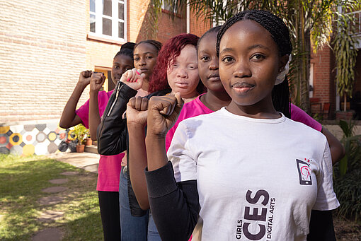 Fünf Mädchen aus Simbabwe steht versetzt hintereinander, schauen in die Kamera, und halten jeweils die rechte Faust hoch
