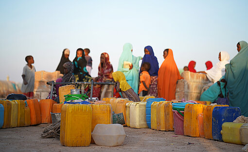 Die im Camp lebenden Familien sind von den Wasserlieferungen abhängig. Eine Reihe Kanister markiert die Reihenfolge der wartenden Frauen und Kinder an der Abholstation.