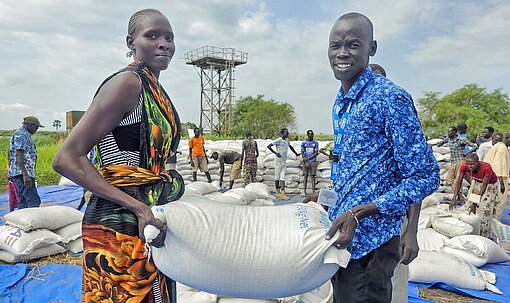 Millionen Menschen in Südsudan sind derzeit auf humanitäre Hilfe angewiesen. Doch der Bedarf ist größer als die von außen gelieferte Unterstützung Eine Frau und ein Mann hieven zusammen einen Sack Getreide von einem Stapel
