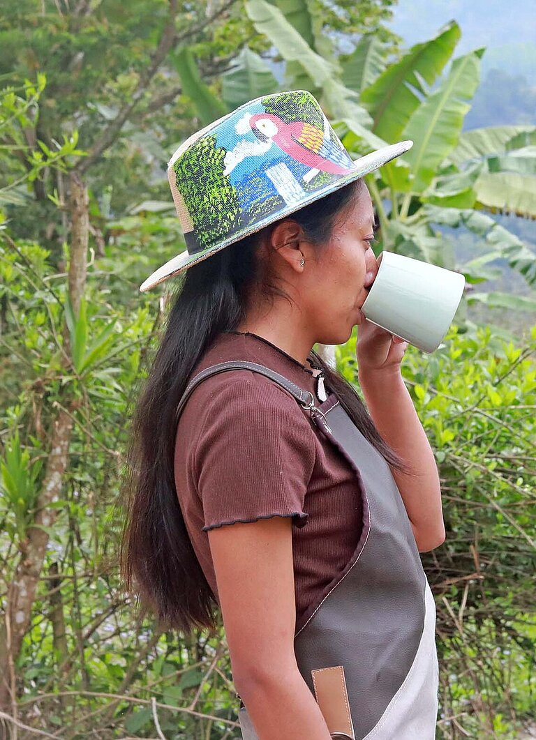 Eine junge Frau steht an einem Waldrand und trink aus einem Becher
