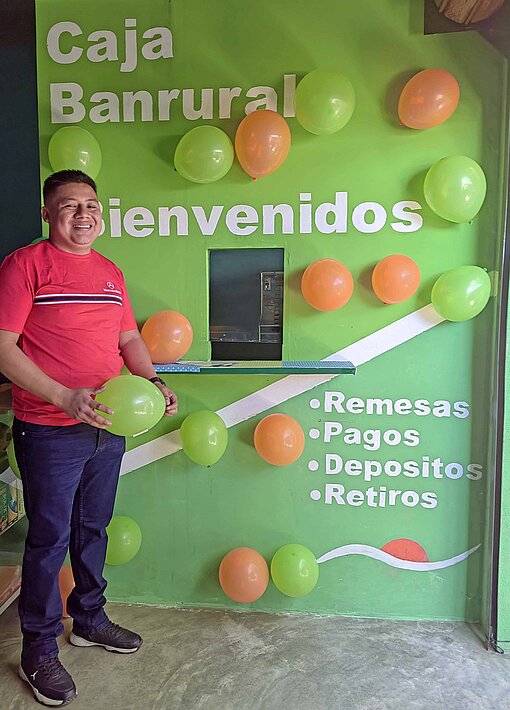 Ein Mann mit rotem Poloshirt steht vor dem Schalter einer kleinen Bank