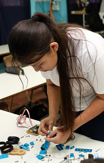 Ein Mädchen ist über einen Tisch gebeugt und schraubt technische Bauteile zusammen