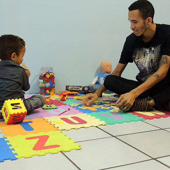 Valnei spielt mit seinem Kind auf Buchstabenteppich.