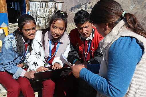 Vier Jugendliche sitzen vor einer Schule zusammen vor einem Laptop.