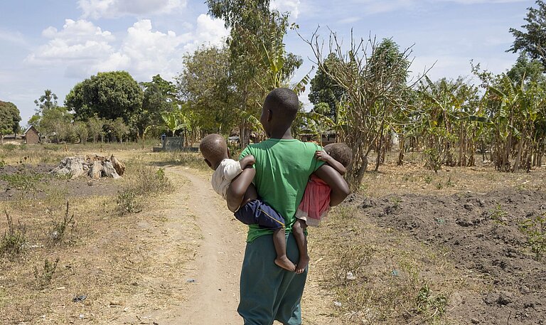 Nalongo geht in ihrer Gemeinde und trägt ihre Kinder in den Armen