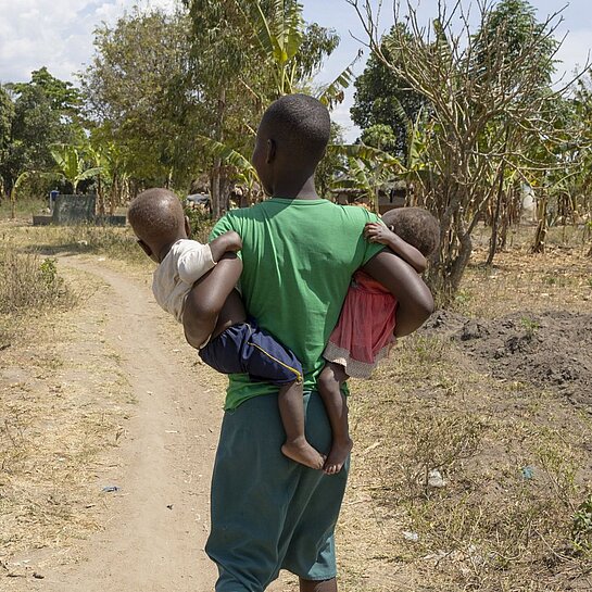 Nalongo geht in ihrer Gemeinde und trägt ihre Kinder in den Armen