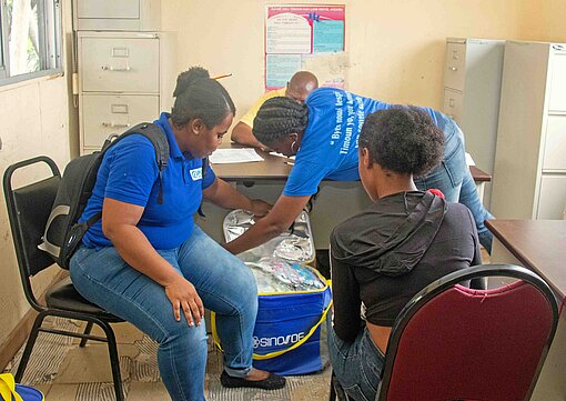 Nathalie (17) und ihr Baby sind vor der Bandengewalt in Port-au-Prince geflohen. Plan-Teams stellen ihr ein Set für die Versorgung ihres Säuglings zur Verfügung Im Plan-Büro werden Nothilfepakete verteilt